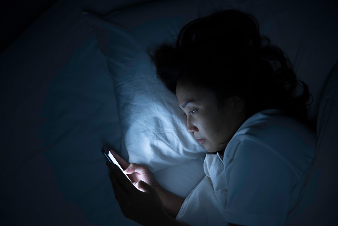 woman on her phone while in bed, blue light on her face