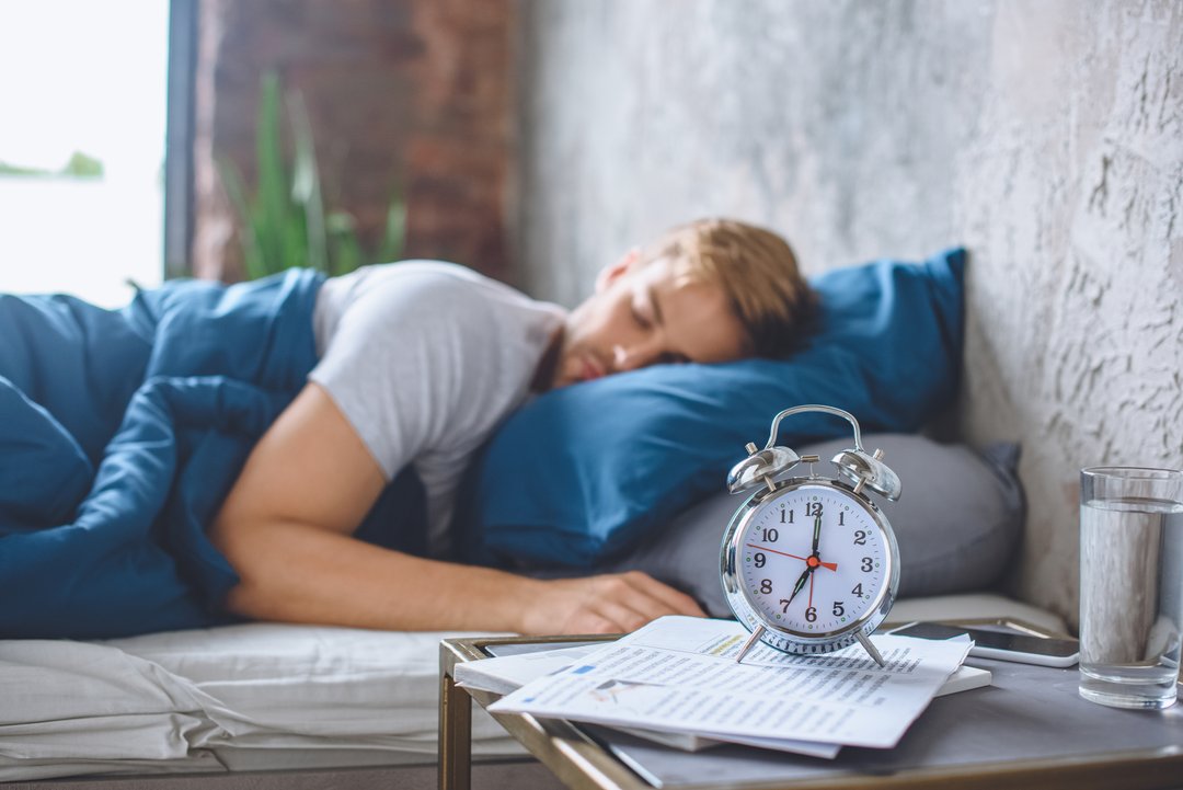 clock next to man sleeping on his bed