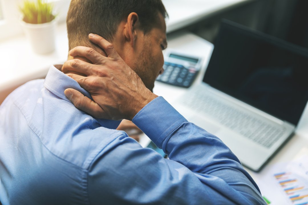 man at his desk, holding hand on neck as he copes with physical discomfort and pain