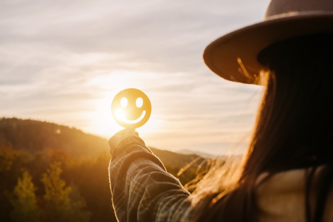 woman holding a happy face sticker to the sun