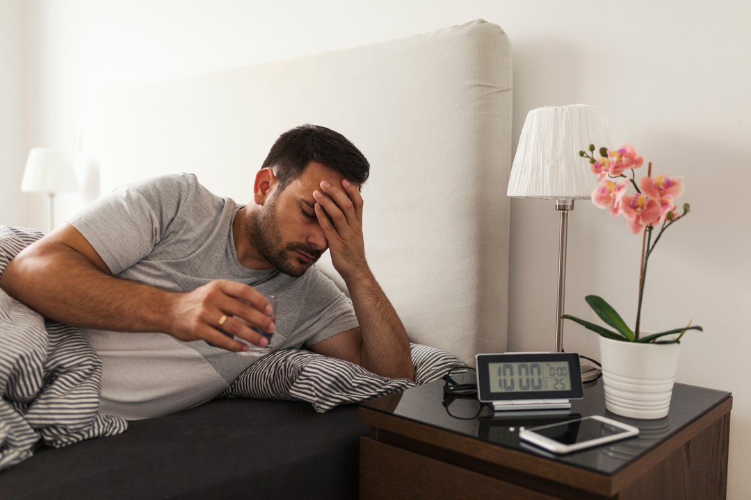 young man in bed with a headache at 10 am hungover from excessive alcohol drinking