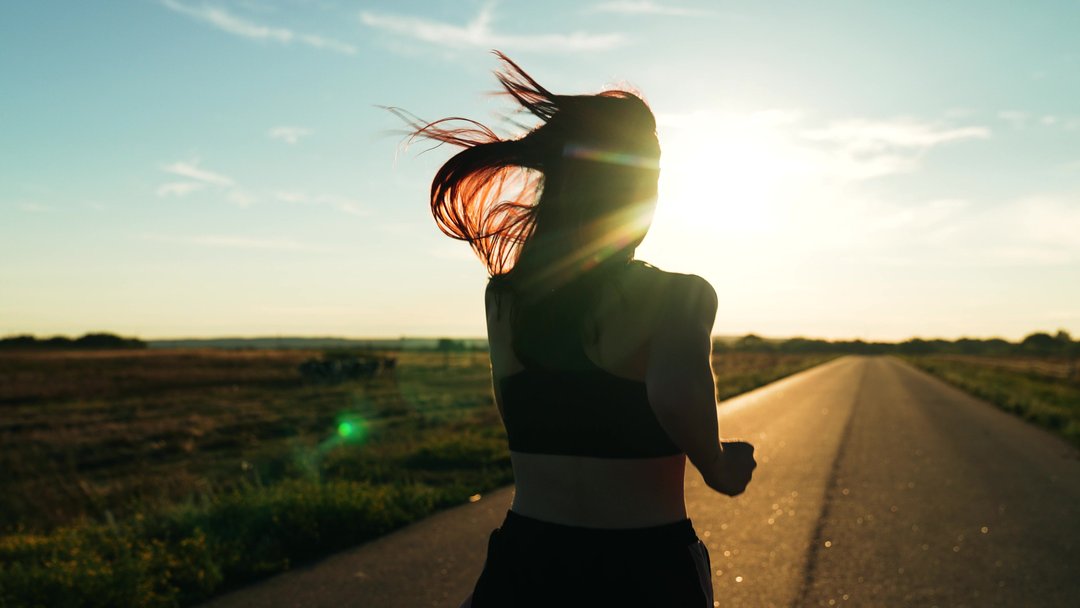 woman running on a long road with the sun in her face