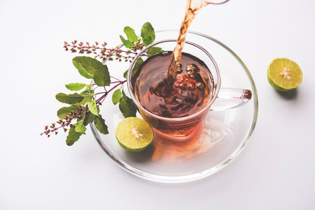 pouring Holy Basil or Tulsi Tea in transparent glass cup with saucer. Popular Ayurvedic medicine from India