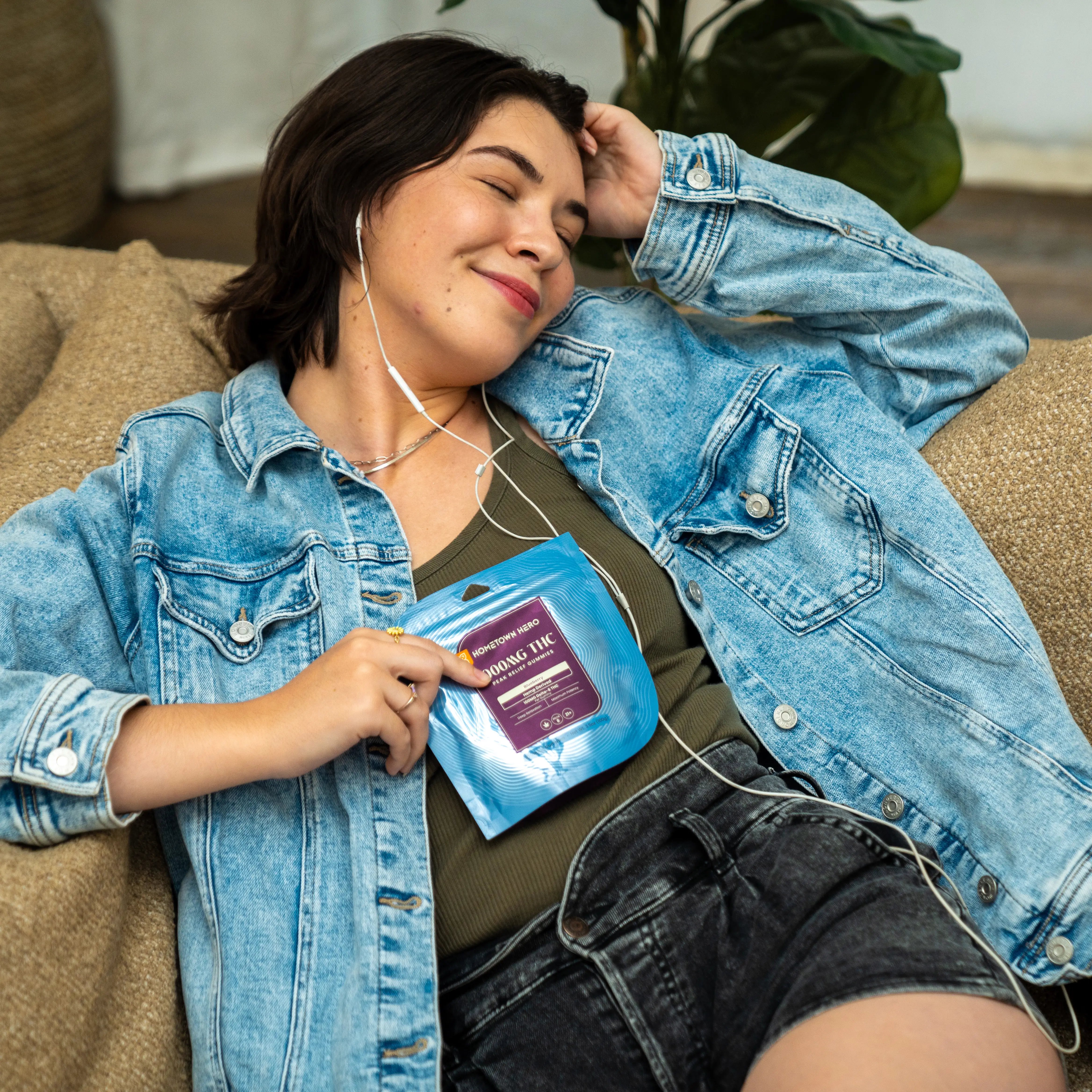 Woman listening to music and smiling with a bag of Hometown Hero gummies