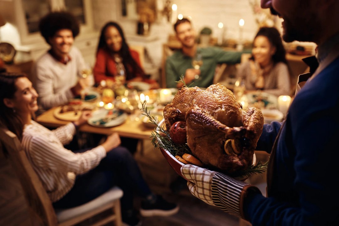 Man bringing a golden roasted turkey to a table of guests at Danksgiving dinner