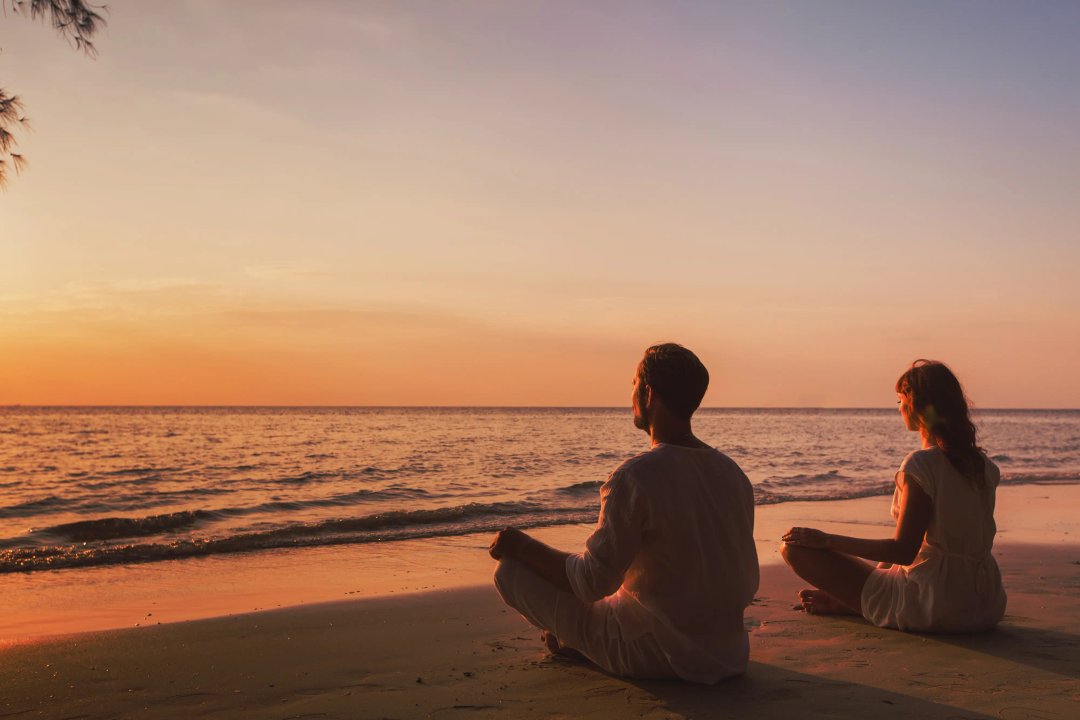 man and woman meditating peacefully at the beach