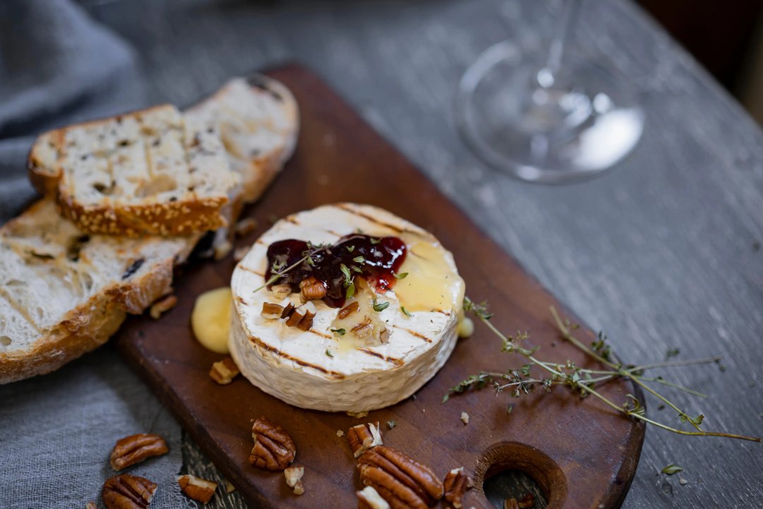 THC-infused baked brie on a cutting board with jam and pecans