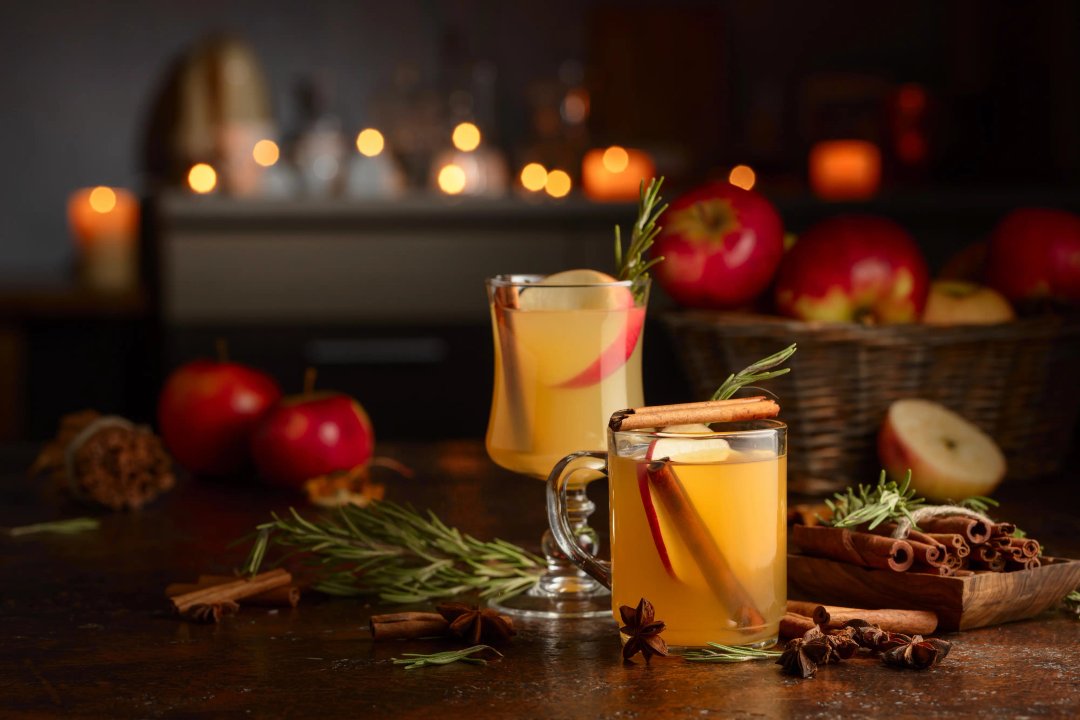 Two glasses of warm spiced cider with cinnamon sticks and apples