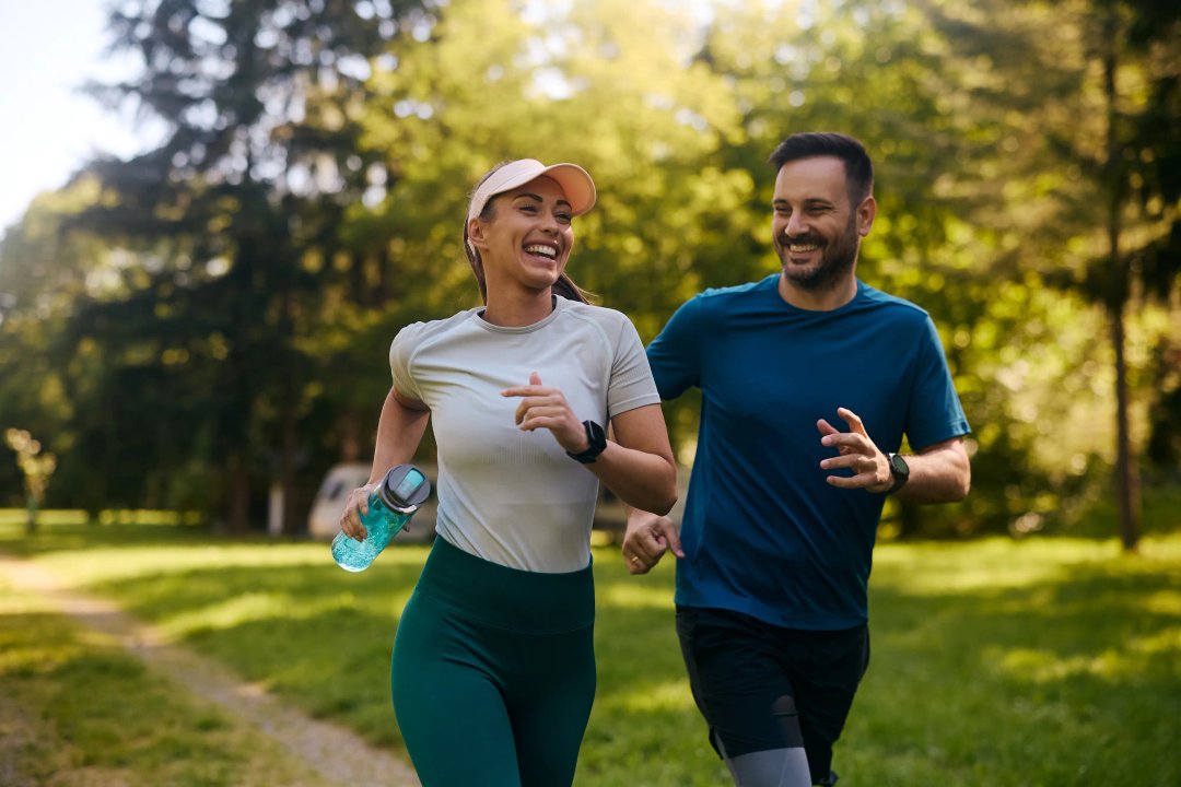 Cheerful athletic couple jogging through park.