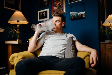 young man exhaling vapor while sitting on his couch