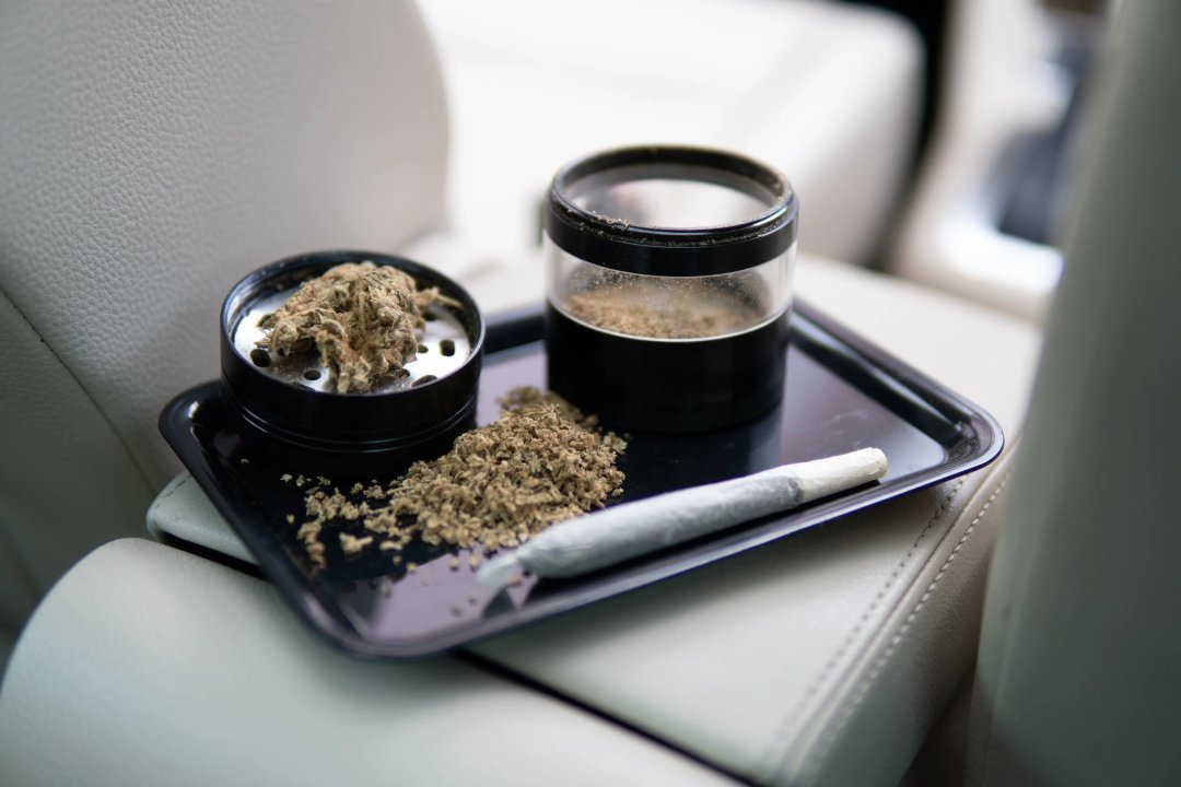 car dashboard with blunt, grinded flower and herb grinder on console