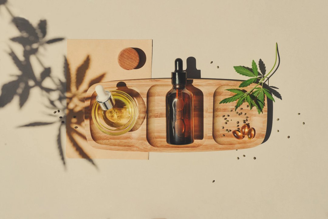 assorted cbd products on a table: capsules, tinctures, oils, and leaves of a hemp plant.