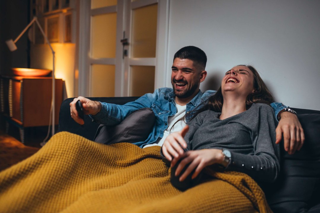 a couple laughing while watching tv together on the couch