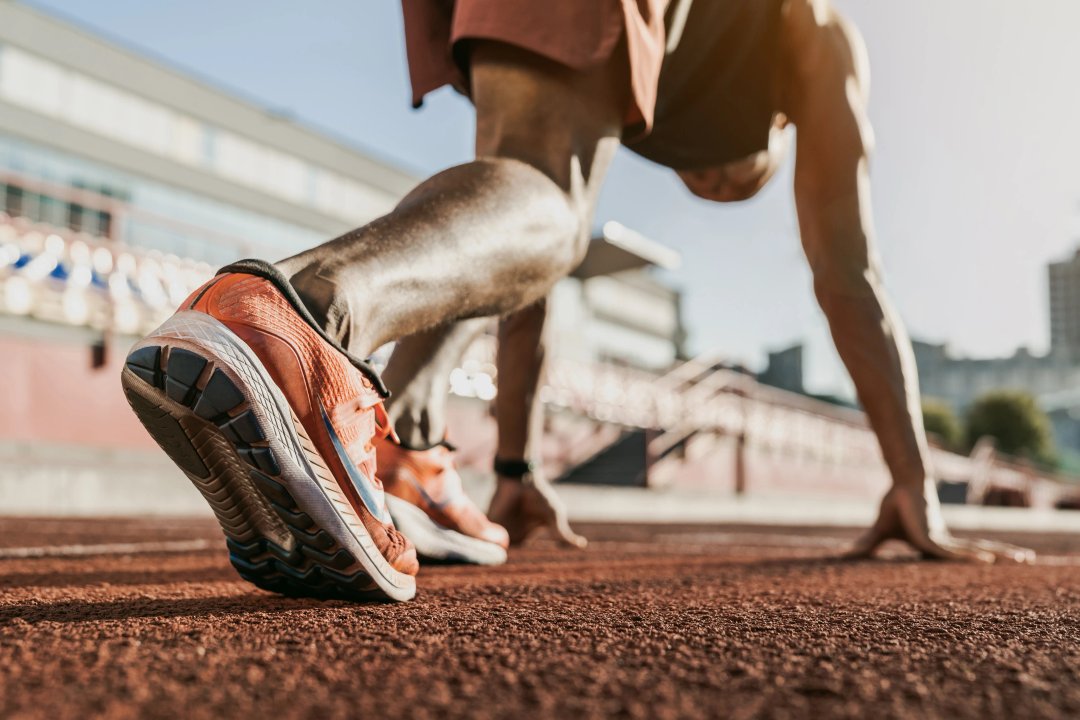 Close up of male athlete getting ready to start running on track . Focus on sneakers