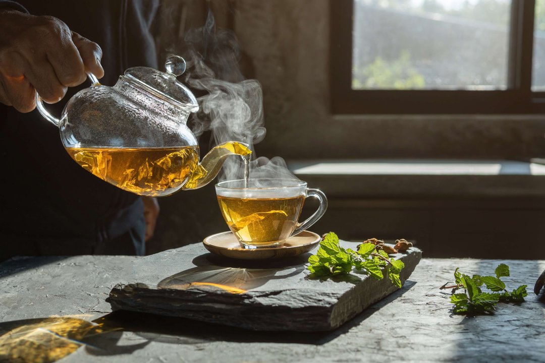 man pouring hot, steaming tea with mint leaves