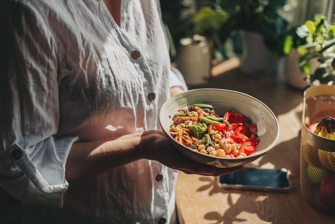 Young woman eating healthy food sitting in the beautiful interior with green flowers on the background