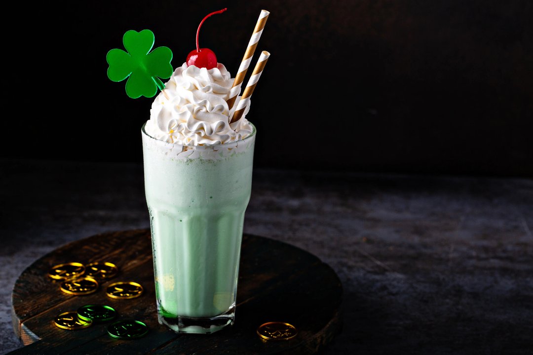 minty shamrock shake with st. patricks day clover and coins and a cherry in a chilled glass