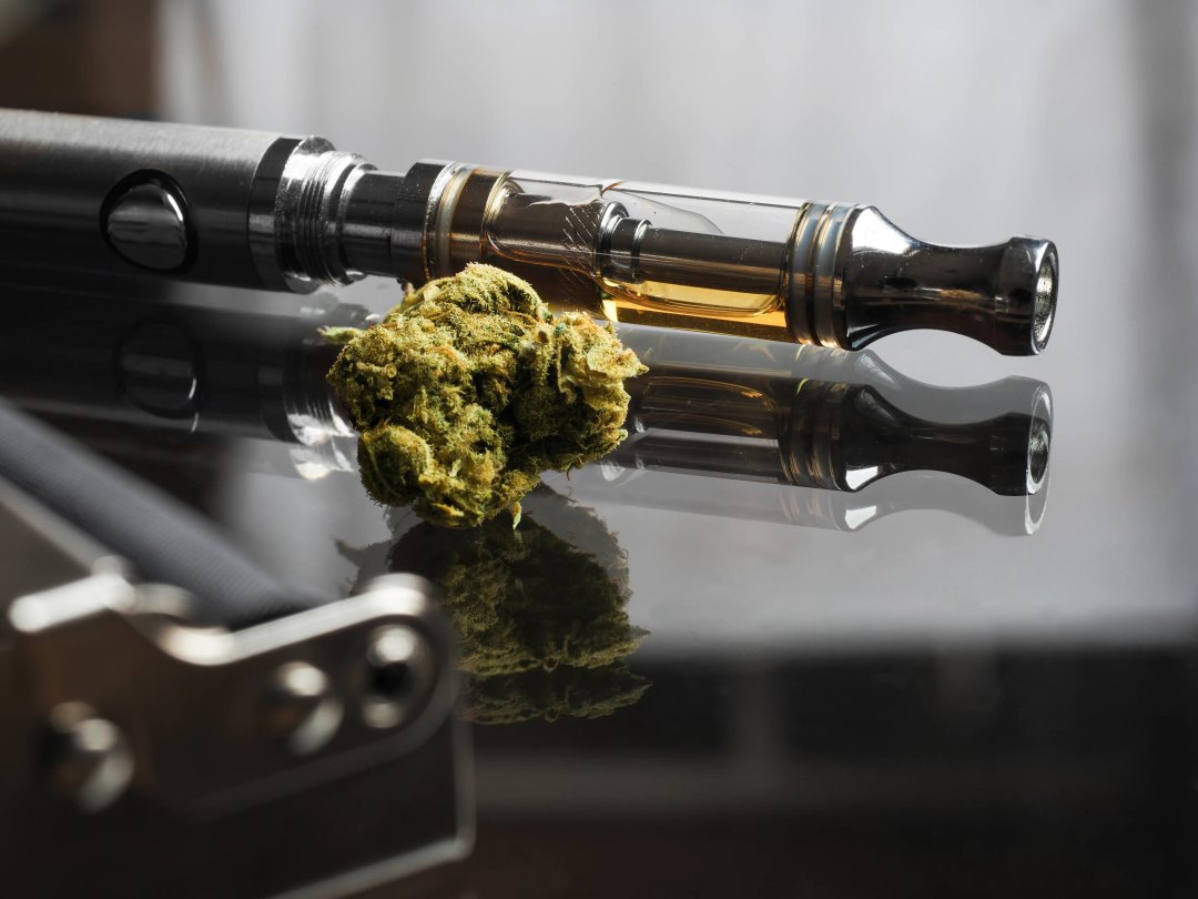 closeup of a vape cartridge with a cannabis bud beside it