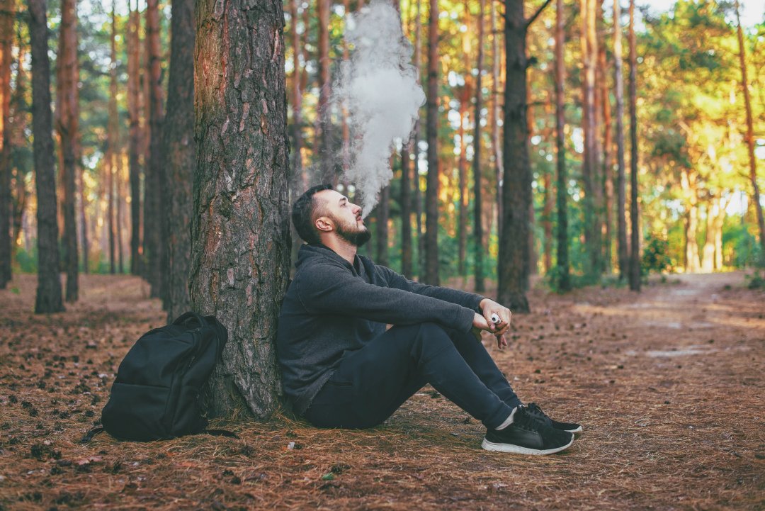 young bearded man vaping outdoors