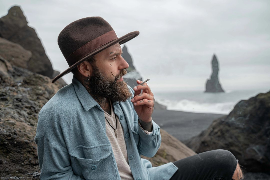 Man smoking weed and blowing puffs of smoke while resting at the foggy beach