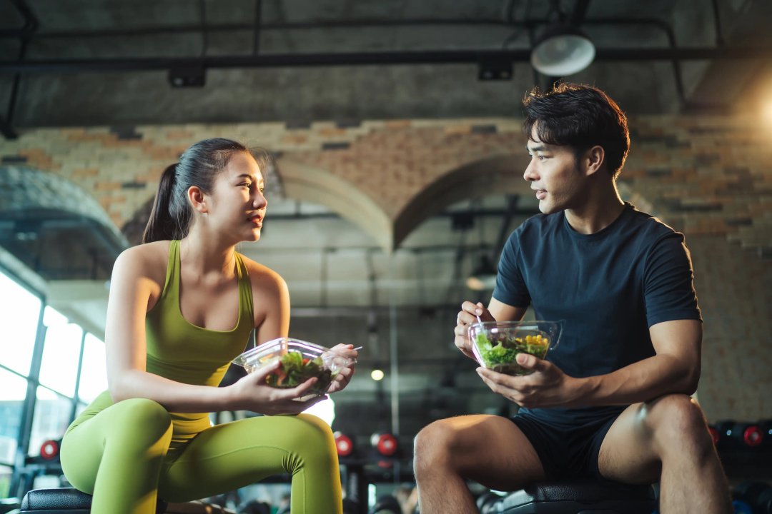 two healthy young individuals in the gym eating healthy meals